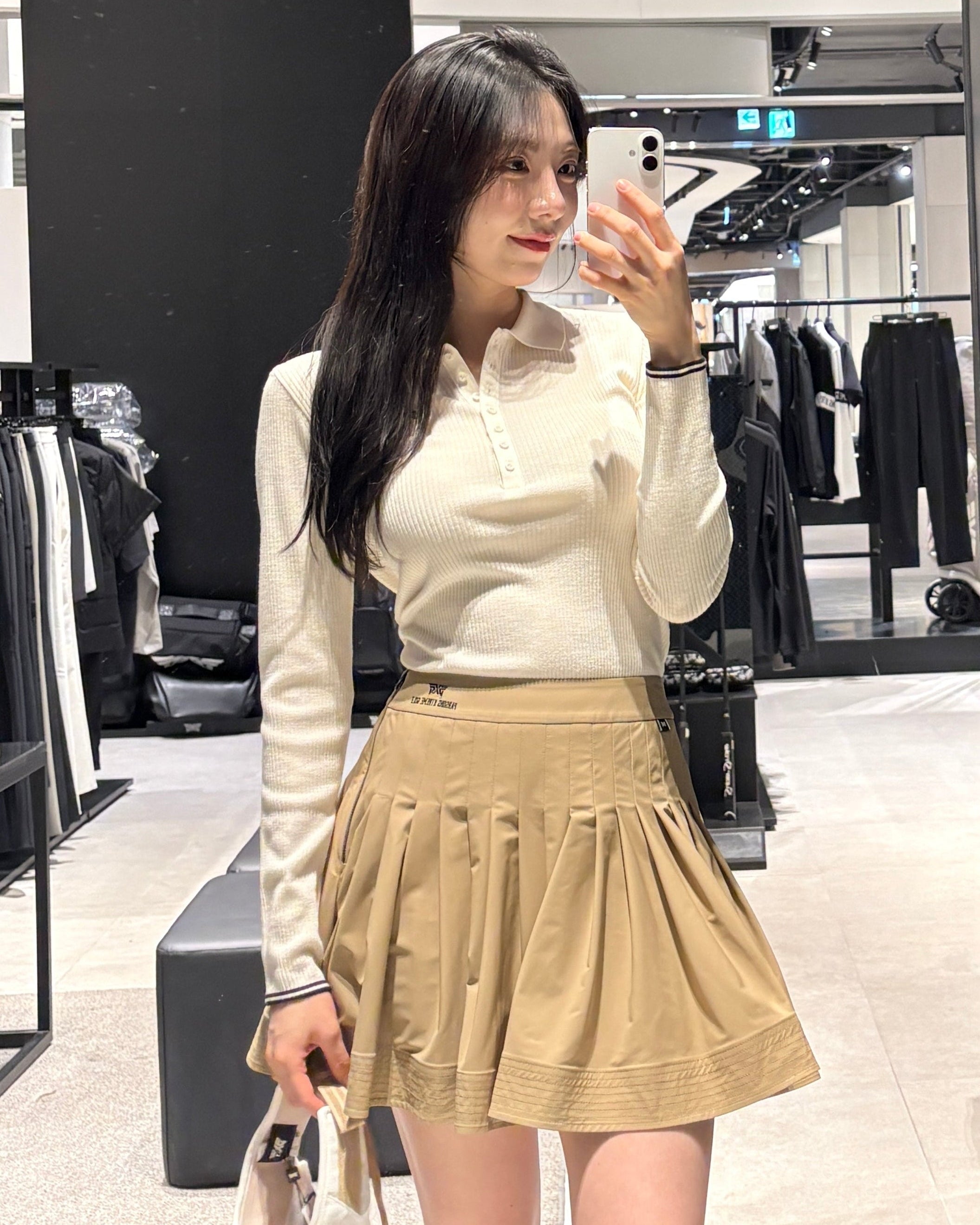 


Woman taking a mirror selfie in a korea golfwear of pxg korea in  department store  wearing a white golf blouse and beige golf skirt.